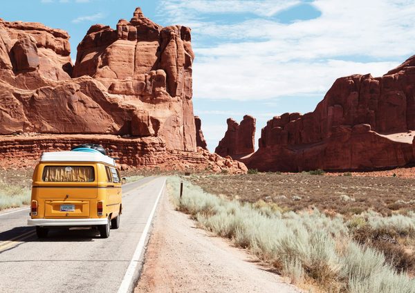 A yellow van on a road between red rock formations
